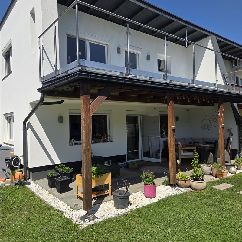 Umlaufendes Glasgeländer an einem Balkon mit Holzstützen